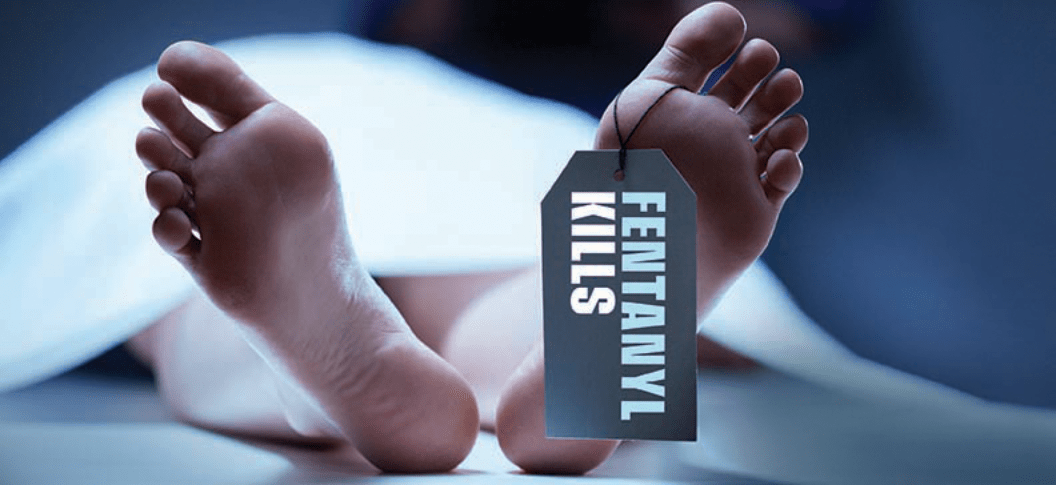 The image shows a pair of bare feet on a morgue table, tagged with 